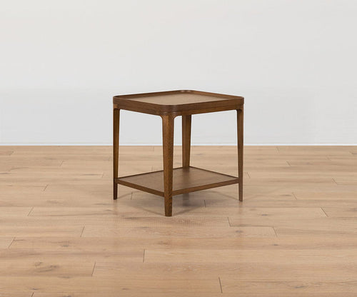 The Aden End Table, a compact square piece crafted from solid oak with slender legs and a lower shelf, is set on a light hardwood floor against a plain white wall.