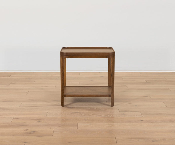 The Aden End Table, featuring a square top and lower shelf, showcases timeless elegance and functional design with its solid oak construction. Part of the Aden Collection, this small wooden side table is perfect for any space, whether placed on a light wood floor or set against a plain white wall.