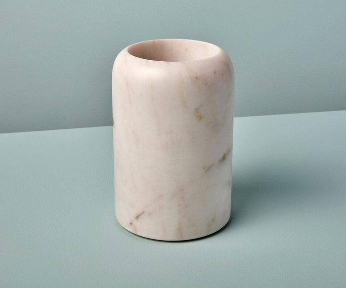 Here’s a rewritten version using the provided product data: The Adia White Marble Bottle Holder—crafted from smooth white marble with subtle brown veining and made in India—rests on a light blue surface against a matching blue background, exuding luxury.