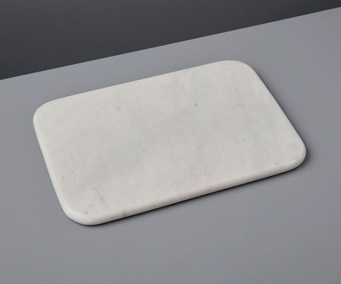 The Adia White Marble Slab, a luxurious rectangular piece with rounded edges, is showcased on a smooth gray surface against a darker gray background. Handcrafted in India from elegant white marble, it elevates any space with timeless sophistication.