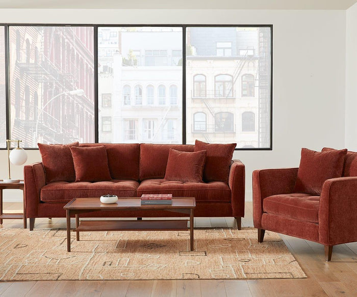 Modern living room with a rust-colored sofa, matching armchair, wooden coffee table, and the Aerlig Table Lamp positioned on the side table. Large windows reveal buildings outside, while a beige rug lies over the wooden floor.