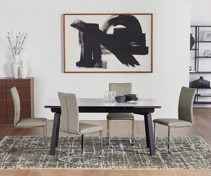 A modern dining area featuring a rectangular table and four Alma Dining Chairs in beige, complemented by abstract black and white wall art, a rug, and minimal decor such as a vase with branches and stacked plates. The space exudes a clean, contemporary style.