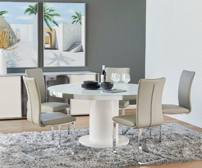 Modern dining area featuring a round white table surrounded by four Alma Dining Chairs in beige, set atop a gray rug. Wall art depicting architectural scenes enhances the contemporary style, while a sideboard displays décor, wine bottle, and glasses beneath soft natural light.