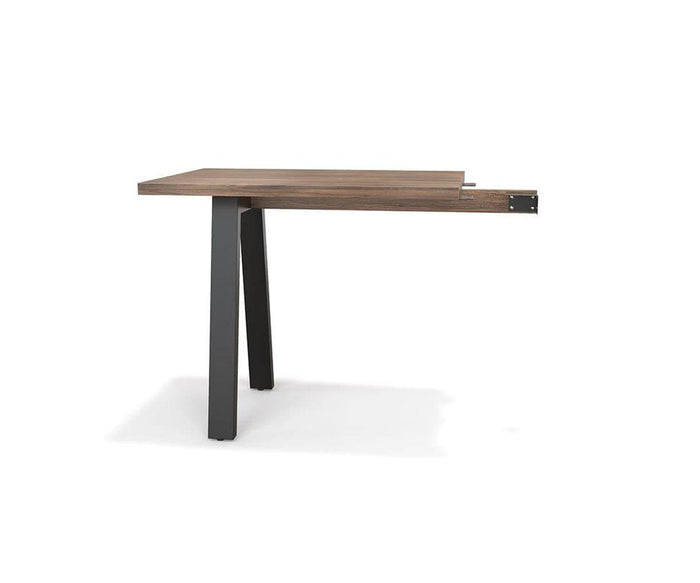 The Arren Return Desk, shown in walnut melamine with two black metal legs and one brown wooden leg, is partially assembled with its tabletop extending over one side against a white background. Made in Italy, this eco-friendly desk blends sophisticated style with sustainable craftsmanship, embodying the signature Arren Return Desk design.