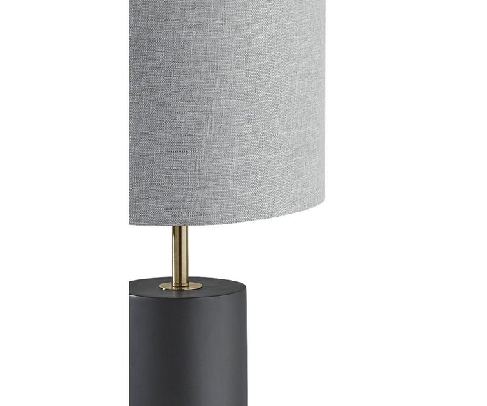 Partial view of the Ash Table Lamp, showcasing its cylindrical dark wood base, gold stem, and light gray fabric lampshade set against a white background.