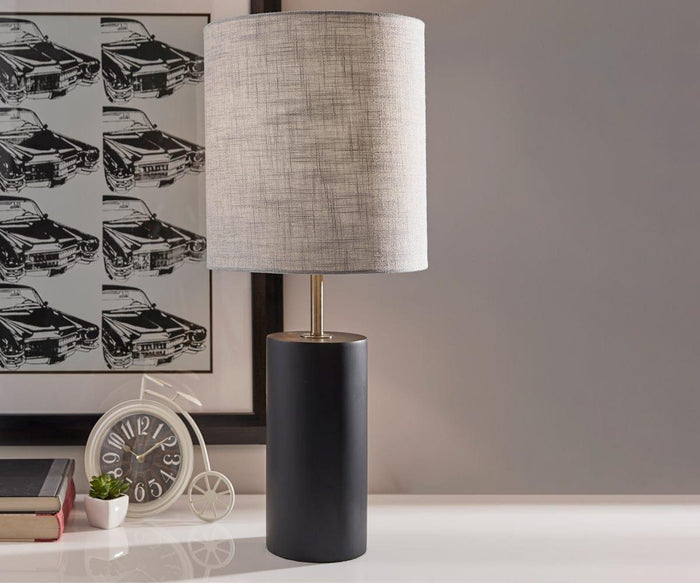 The Ash Table Lamp, featuring a dark wood base and a textured light gray shade, sits on a white desk near a small clock, books, a plant, and framed artwork of classic cars.