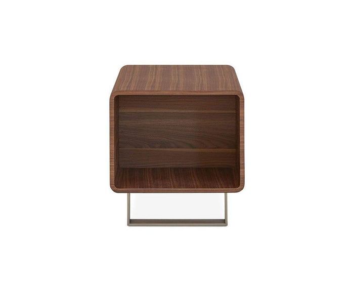 A modern wooden Baptisia End Table in a rich walnut finish features an open rectangular shelf, rounded edges, and a metal base, photographed against a white background. Its striking form evokes the lines of cubist art sculpture, blending both function and artistic flair.