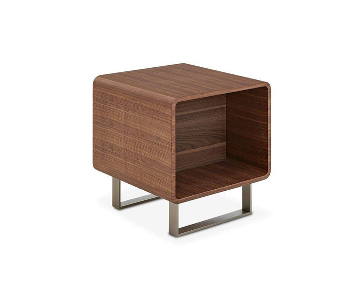The Baptisia End Table is a modern wooden nightstand featuring a smooth cherry finish, rounded edges, an open front shelf, and sleek metal legs—its striking cubist-inspired lines are displayed against a white background.