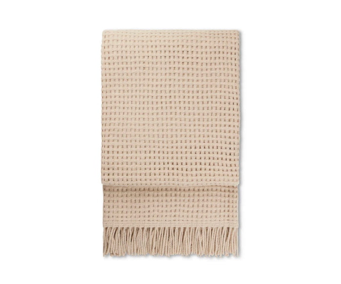 The Basket Throw, shown folded on a white background, features a beige woven design crafted from recycled alpaca wool with a subtle grid-like texture and long fringe along the bottom edge. Cozy and stylish, this throw is ideal for bringing warmth and elegance to any room.