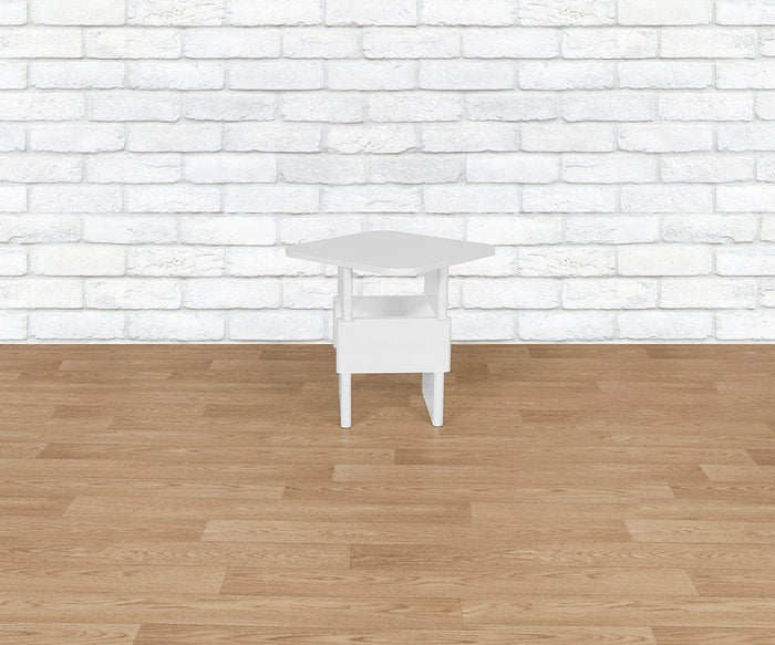 The Batia Side Table, featuring a small white hexagonal design with a lower shelf and drawer, is placed on a wooden floor in front of a white brick wall.