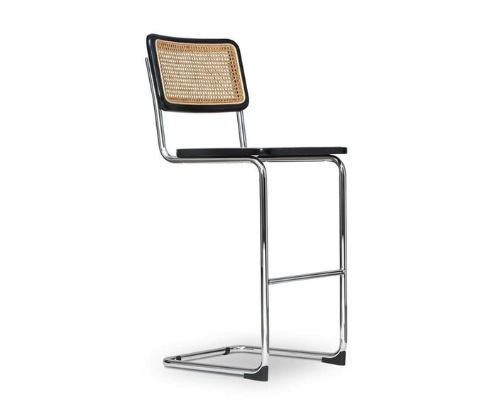 Introducing the Bendt Bar Stool—a modern piece featuring a tubular chrome frame, a sleek black seat, and a woven cane backrest crafted from European beech wood. Its cantilever design, which omits back legs, echoes the minimalist and contemporary style of classic mid-century bar stools.