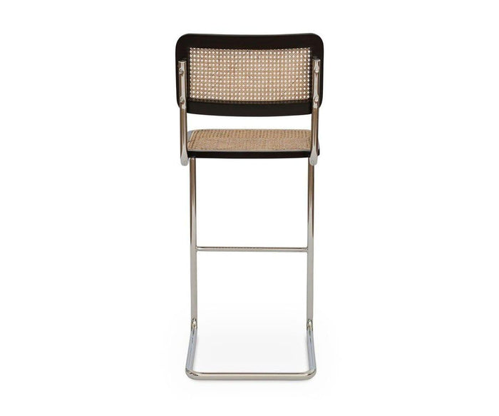 The Bendt Bar Stool, featuring a modern mid-century design with a metal cantilever frame, woven cane seat and backrest, and dark European beech wood accents, is shown from behind against a white background.