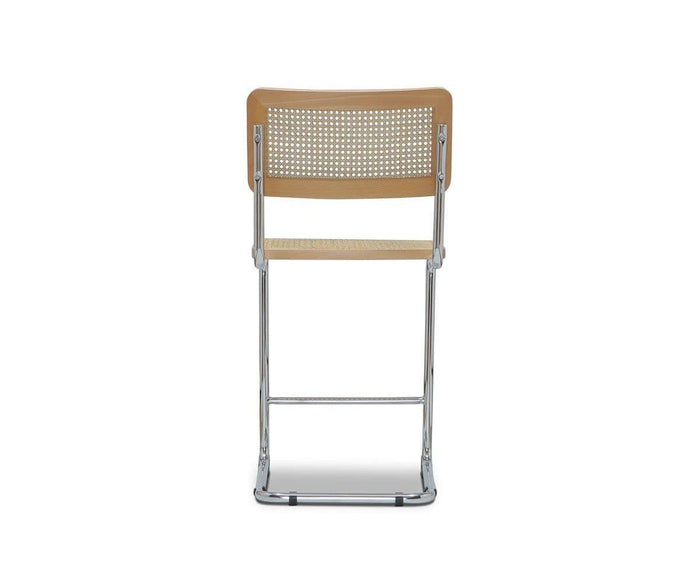 The Bendt Counter Stool is shown from the back against a white background. This beige chair features a chrome metal frame and a perforated cane seat and backrest, with a sleek, minimalist design inspired by mid-century aesthetics.