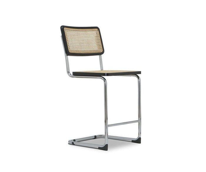 The Bendt Counter Stool is a modern cantilever chair with a chrome frame and woven cane seat and backrest. Designed without armrests, it features a minimalist, mid-century aesthetic reminiscent of iconic counter stools. The product is set against a plain white background.