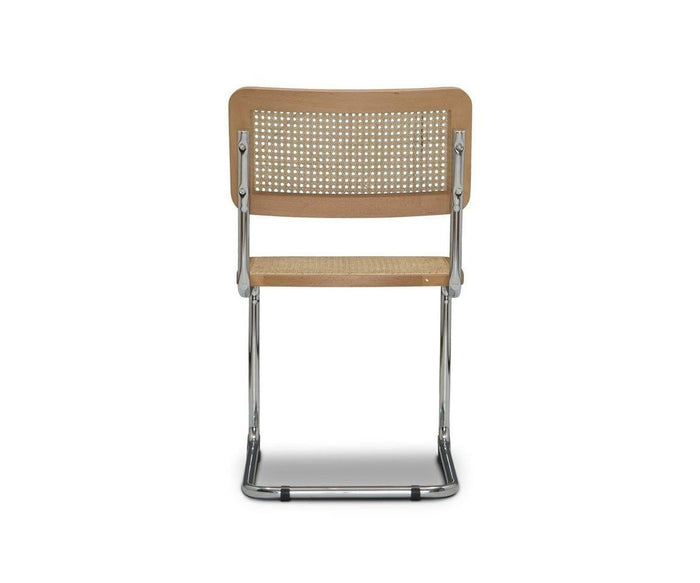 The Bendt Dining Chair is a stylish mid-century piece featuring a cane seat and backrest elegantly viewed from behind. Its shiny chrome frame highlights a classic cantilever design, while beech wood accents evoke timeless sophistication. Set against a plain white background, the Bendt Dining Chair epitomizes modern vintage appeal.