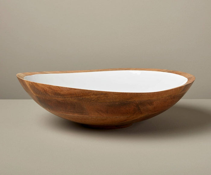 The Bright Bowl, crafted from mango wood with a spacious, shallow design and an irregular edge, features a white interior and sits on a light grey surface against a plain beige background—blending sustainable style with the timeless charm of handcrafted serveware.