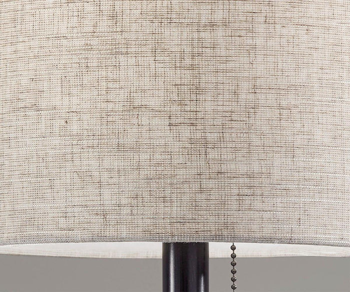 Close-up of the Cara Floor Lamp, showcasing a beige fabric shade with a textured finish and a visible pull chain hanging from its bottom edge, all supported by a dark metal base.