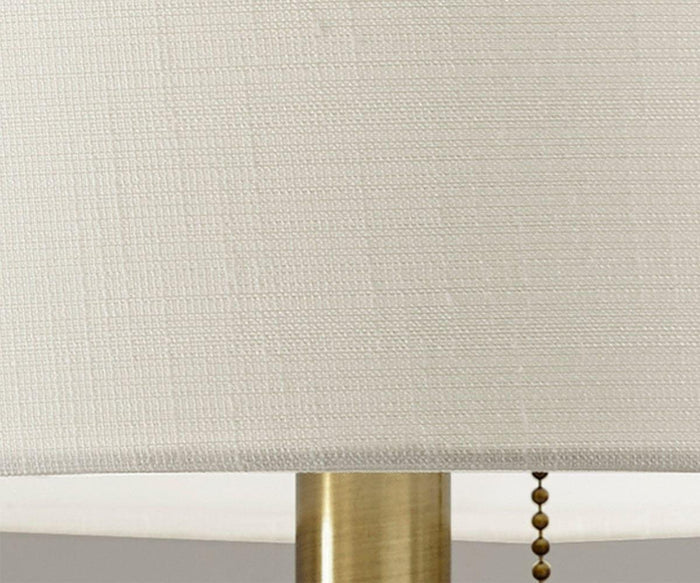 A close-up of the Cara Table Lamp featuring a textured fabric shade, with part of its metal base and a small pull chain visible.