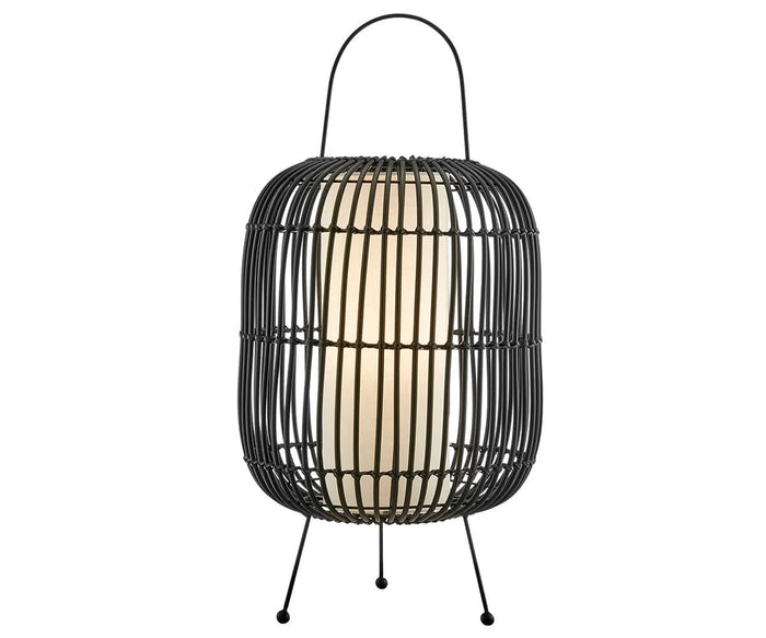The Clement Table Lamp in black features a modern design with a rounded wire frame, three slim legs, a top handle, and a white cylindrical cordless light inside that is battery-powered and evokes the look of faux rattan.