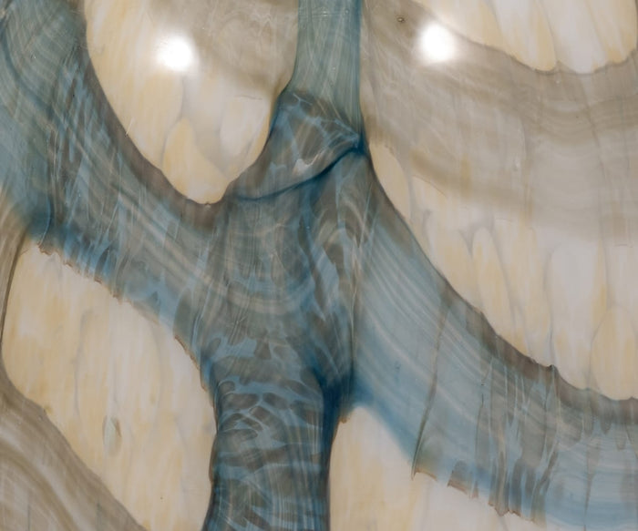 Close-up of a polished stone surface featuring swirling beige, blue, and gray patterns, illuminated by two bright reflections from overhead lighting—evocative of the refined textures seen on the handcrafted Coastal Agate Vase, making it a remarkable decorative accent.