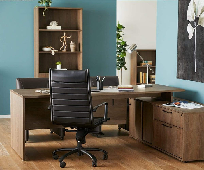 A modern office featuring a wooden desk, black swivel chair, shelves with decor, the Collette Desk Lamp with USB Port for added convenience, and cabinets. The room has blue walls, wooden flooring, and a large flower painting.