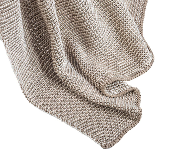 A Cooper Clay–colored knitted blanket draped in soft, wavy folds, with detailed textured stitching throughout the fabric—crafted from cotton yarn for a retro-cozy feel, this is the inviting Cooper Throw.