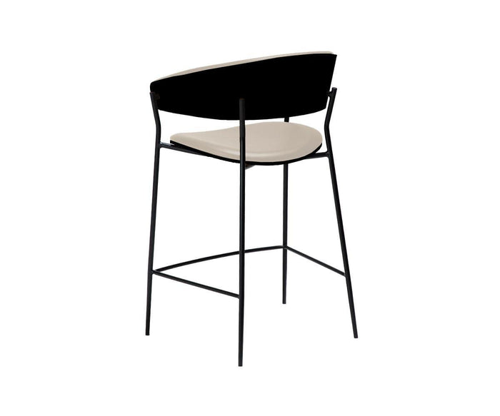 The Crib Leather Counter Stool features a contemporary design with a sleek black metal frame, a curved black backrest, and a light beige cushioned seat, displayed against a plain white background.