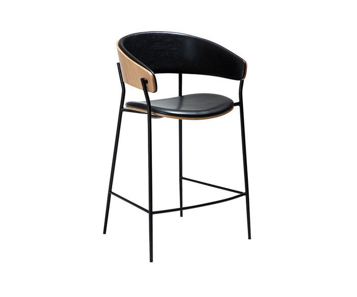 Introducing the Crib Leather Counter Stool, featuring a sleek black metal frame, luxurious black leather seat and backrest, and elegantly curved wooden paneling on the backrest. Set against a white background, this modern stool effortlessly blends style and comfort for any space.