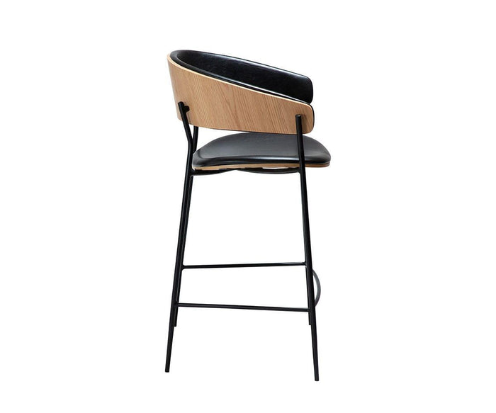 The Crib Leather Counter Stool features a sleek black metal frame, a gently curved wooden backrest, and a cushioned black leather seat. Shown from a side view against a white background, this contemporary bar stool exemplifies modern design.