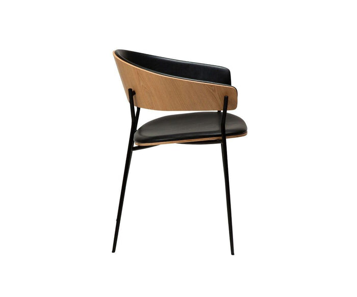 The Crib Leather Dining Chair features a curved wooden backrest, a black leather cushioned seat, and slim black metal legs, seen from the side against a white background—this contemporary piece brings sophisticated style to any modern space.