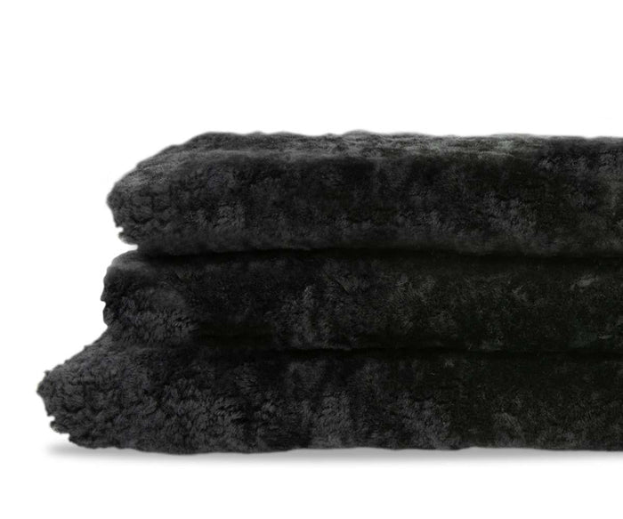 Two plush Curly Double Pelt - Black faux fur throws are stacked neatly against a white background, showcasing the luxurious softness of sheepskin—an essential Scandinavian accent for cozy interiors.