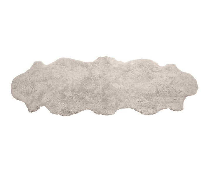 The Curly Double Pelt - Oatmeal is a long, irregularly shaped shaggy rug in a light oatmeal hue, featuring wavy edges reminiscent of an animal hide. Expertly crafted from luxurious New Zealand wool, it is beautifully displayed on a white background.