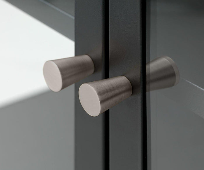 Close-up of two cylindrical brushed metal cabinet knobs on the tempered glass door of the Dion Low Cabinet, their reflections visible in the glass. The knobs are mounted on a dark-colored frame, contributing to the cabinet’s sleek and modern storage solution.