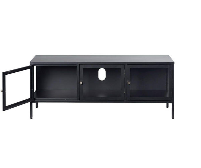 The Dion Media Stand features a modern black metal design with three front tempered glass doors, one of which is open. Its central section includes a circular cable management hole on the back panel, and the stand is supported by four slim legs.