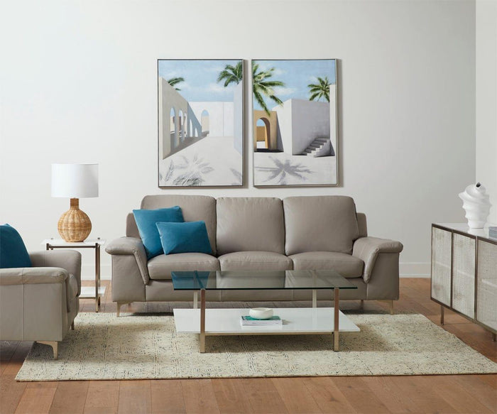 Modern living room with a gray sofa, blue and white accent pillows, a glass coffee table, an armchair, a lamp, and wall art featuring the Distant Escape II Oil Painting—a hand-painted canvas depicting palm trees and Mediterranean architecture that adds an artistic, tropical cityscape touch to the space.