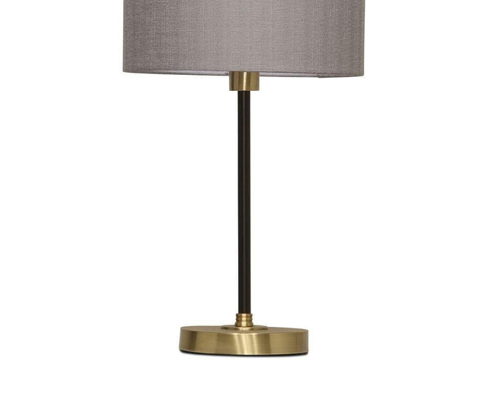 Introducing the Doren Table Lamp: a modern accent for any space, showcasing a brass base, slim black stand, and a cylindrical gray fabric lampshade. Set against a crisp white background, this elegant table lamp seamlessly combines contemporary design with classic style.