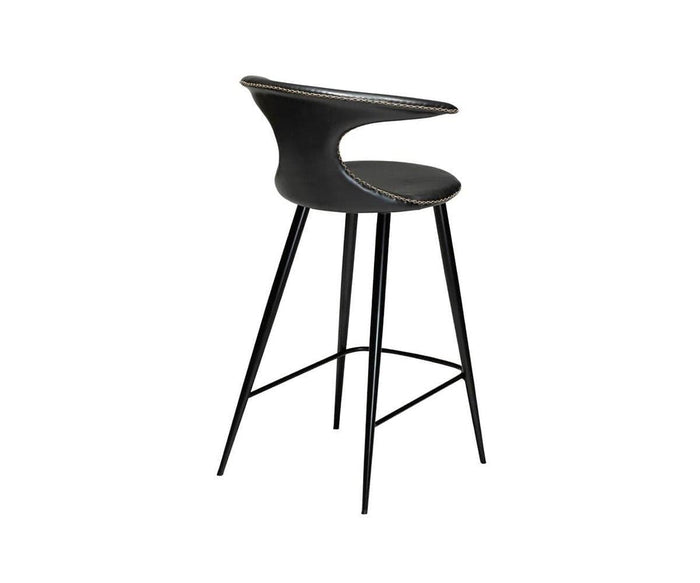 The Drake Counter Stool, featuring sleek black faux leather upholstery inspired by modern Danish design, showcases a curved backrest, slim metal legs with a footrest, and is positioned against a plain white background.