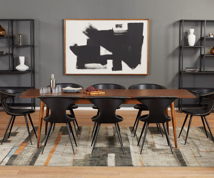 Modern dining room with a wooden table, eight Drake Dining Chairs, abstract black-and-white art on the wall, shelves with decorative items, and a patterned rug on a wood floor.