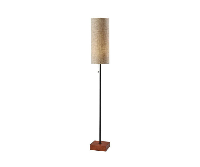 The Dusk Floor Lamp features a cylindrical taupe fabric shade, a slender black metal pole, and a square walnut base. Shown illuminated against a plain white background, this tall lamp adds an elegant touch that perfectly complements mid-century decor.