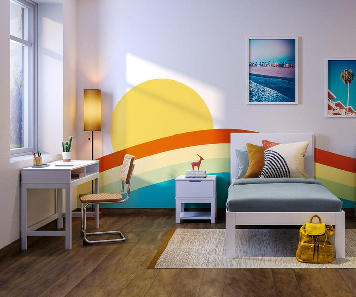 A bright bedroom with a rainbow mural, sun, white bed, yellow pillows, nightstand with a walnut base, desk with chair, window, framed photos on the wall, and a yellow bag on the floor—perfectly accented by touches of mid-century decor and the stylish Dusk Floor Lamp for a cheerful retreat.