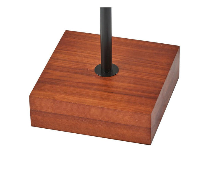 A close-up of the Dusk Floor Lamp’s square walnut base with a central vertical black metal pole, featuring mid-century inspired design, isolated on a white background.