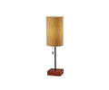 The Dusk Table Lamp features a tall, cylindrical amber fabric shade, a black metal stem, and a square walnut base that effortlessly complements mid-century decor. A small pull chain hangs below the shade. The lamp is photographed against a plain white background.