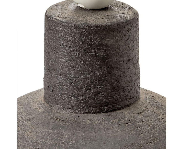 Close-up of a textured, dark gray, cylindrical object with a rough, stone-like surface against a white background, reminiscent of an Earthenware Jug Lamp.