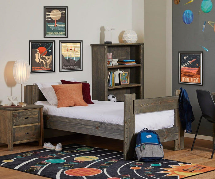 A child’s bedroom with space-themed decor, a wooden bed and furniture, books on a shelf, framed space posters, and a colorful solar system rug on the floor. On the nightstand sits the Egg Table Lamp with its white pleated shade and satin steel base.