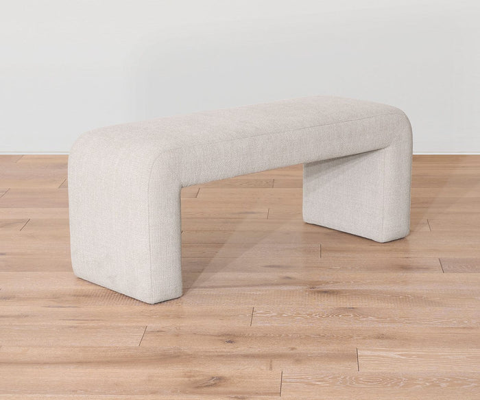 The Eilir Full Bench, featuring a modern minimalist design with rounded edges, sits on a light wood floor against a plain white wall, providing extra seating and a touch of contemporary flair to the space.