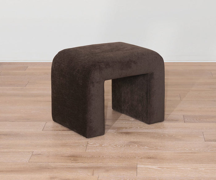 The Eilir Half Bench, featuring a dark brown velvet upholstery and an arch-shaped design, adds contemporary flair as it sits on a light wooden floor against a white wall.