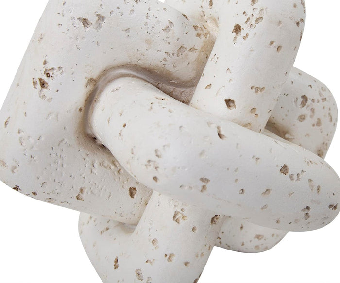 A close-up of the Everlink Sculpture, a white, textured ceramic piece featuring two interlocking geometric forms with a weathered, speckled surface and a travertine-like texture reminiscent of natural stone carving.