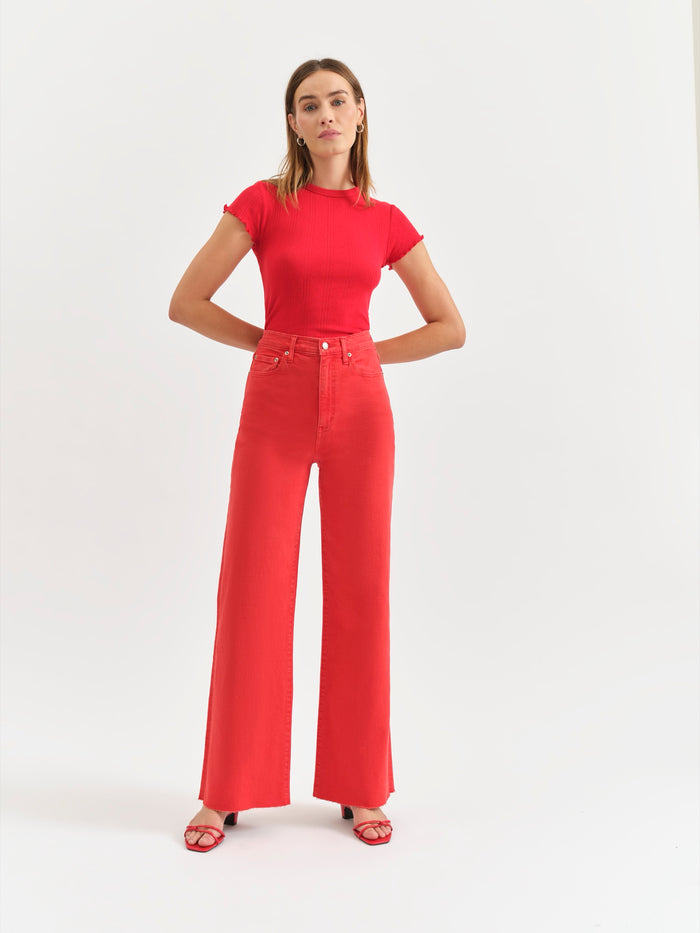 A person standing wearing high-rise wide-leg cherry red jeans and a matching red short-sleeved t-shirt, with feet positioned slightly apart wearing open-toe flat sandals.
