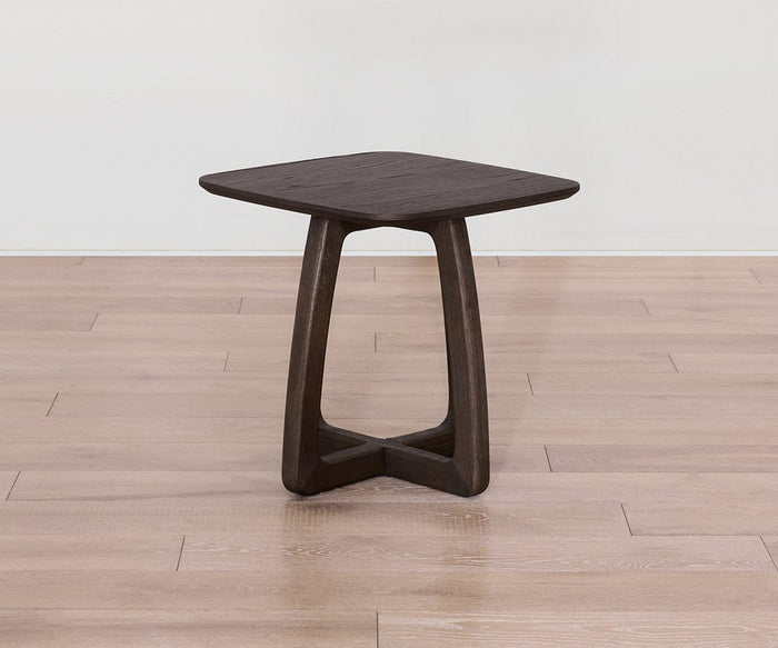The Faroe Square End Table, featuring a smoked oak veneer top and a triangular base, sits on a light wood floor against a plain white wall.