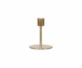 The Fina Candlestick, handcrafted from gold metal, features a round flat base and a single vertical stem designed to hold one candle, displayed against a plain white background.